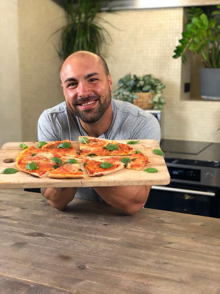 Der Trainer präsentiert mit einem Lächeln im Gesicht eine frisch gebackene Pizza.